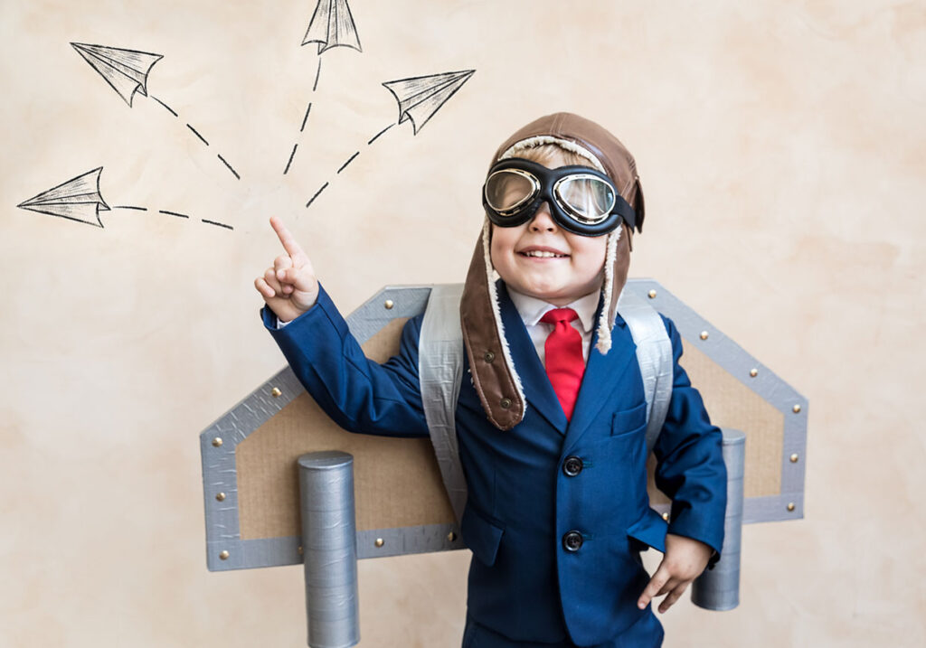 Child standing with a makeshift set of wings and illustration paper aeroplanes